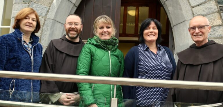 A woman in a green coat, two monks, a woman in a polka dot shirt and a woman in a navy coat stand together for a picture