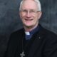 Picture of Bishop Ray Browne, with a cross around his neck, against a black background.