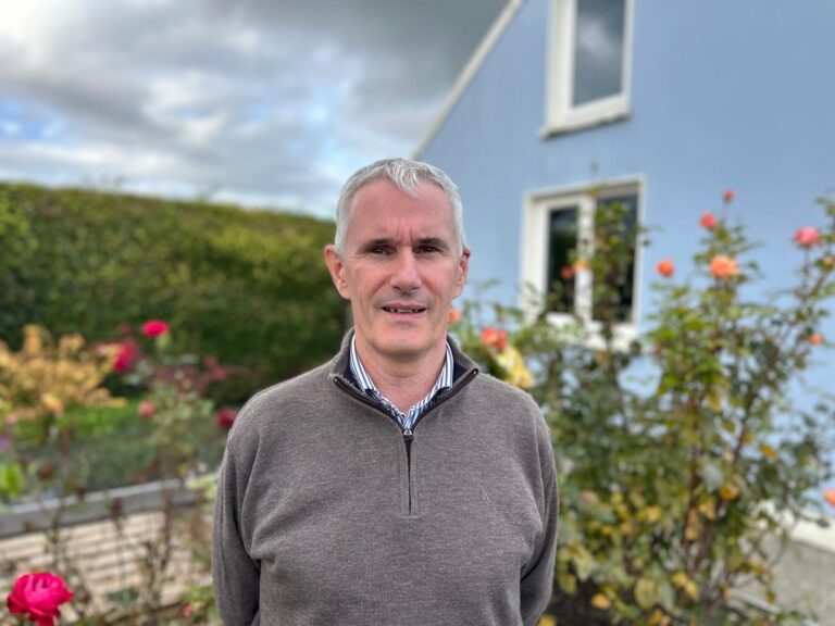 Image of a man in a grey jumper standing in flower garden